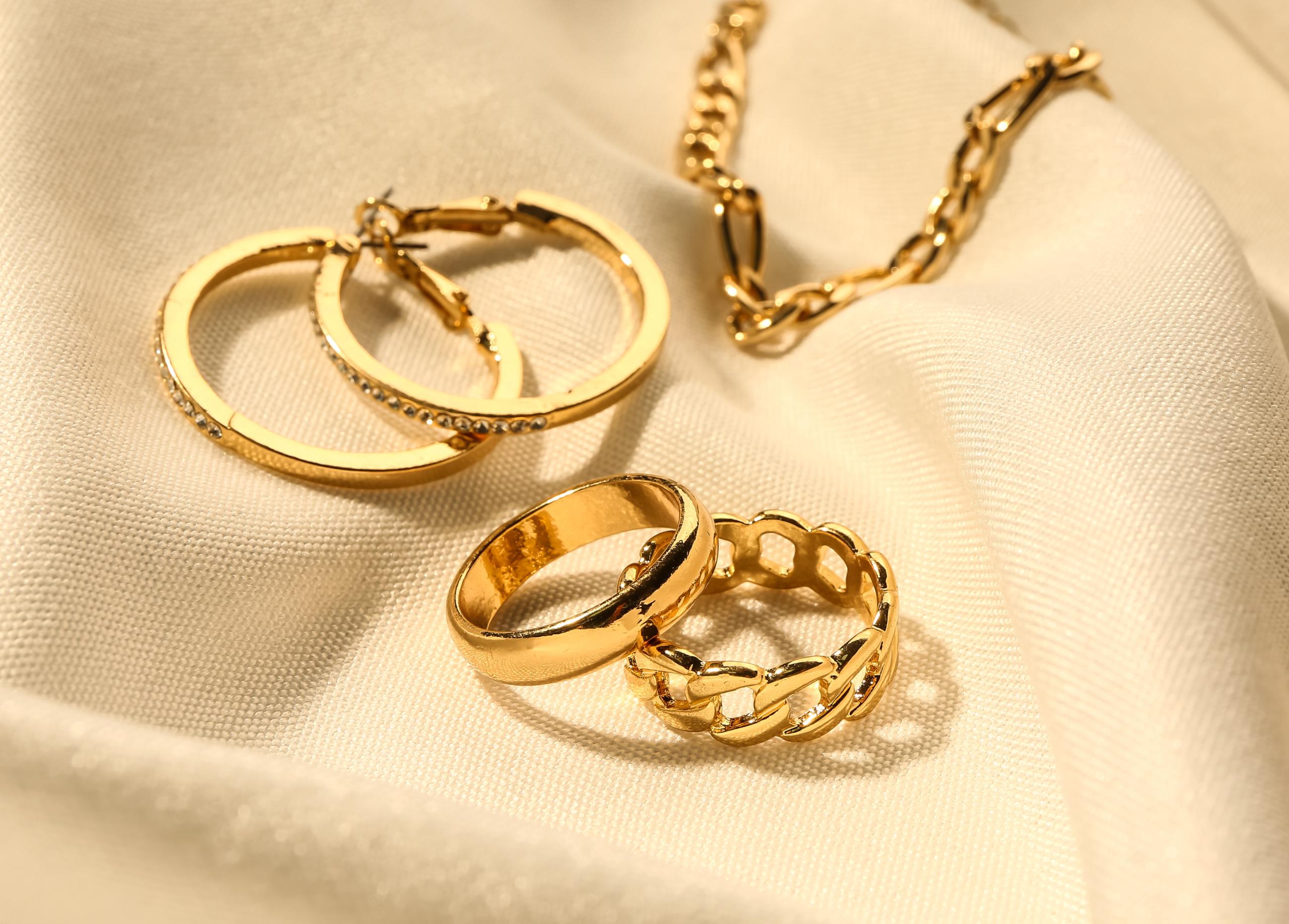 Close-up of gold hoop earrings, rings and chain jewellery arranged on cream fabric