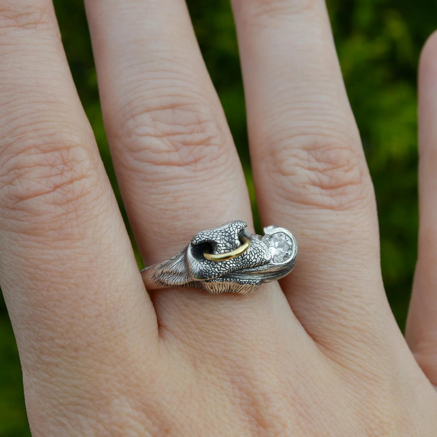 Close-up of a hand wearing a sculptural silver bull’s nose ring with textured nostrils, a small gold hoop and a clear gemstone held by the curling tongue