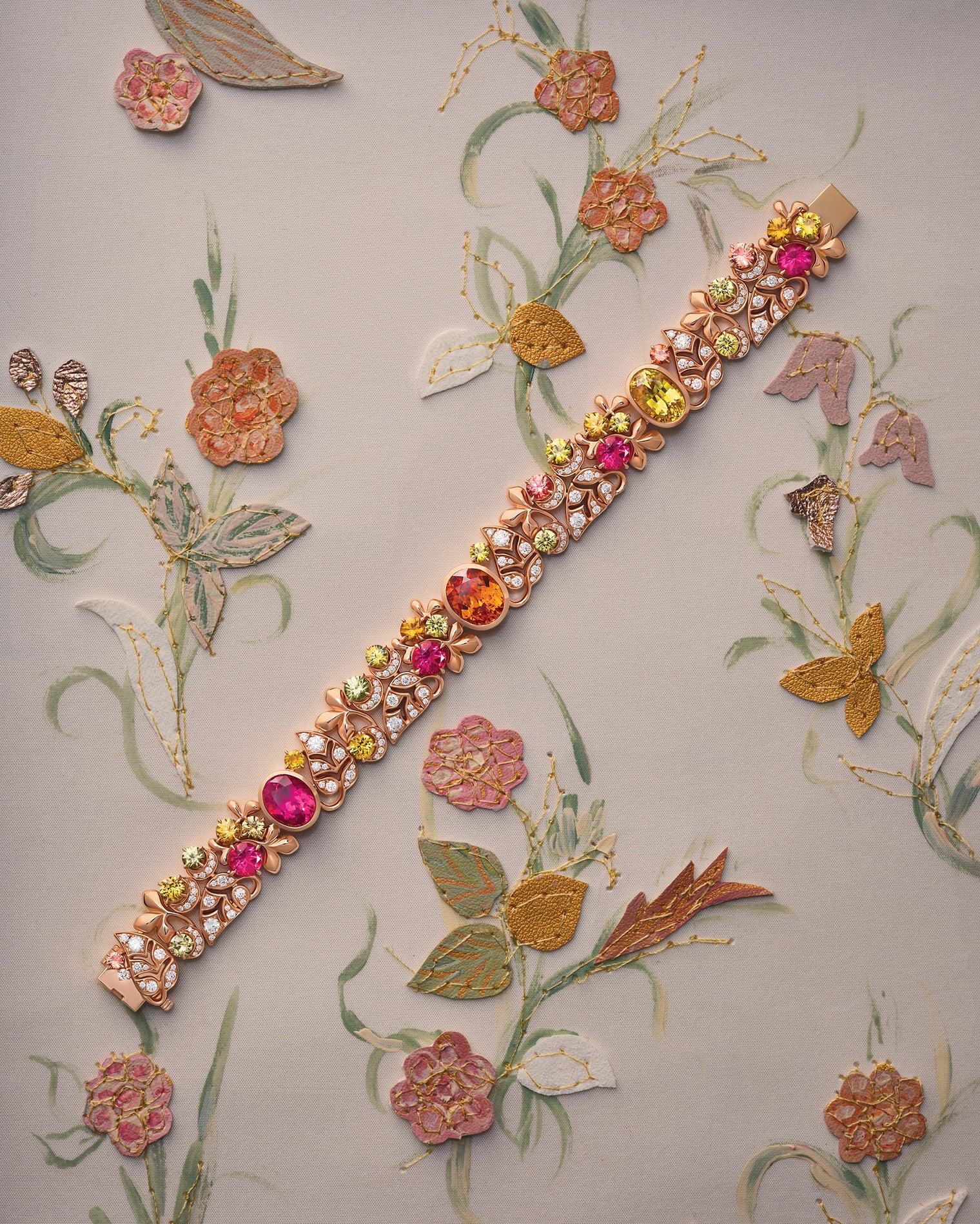The Silk Mantua bracelet by Boodles, featuring pink tourmalines, mandarin garnets, sapphires and diamonds set in rose gold, displayed against a backdrop inspired by the floral embroidery of an historic Spitalfields silk gown.