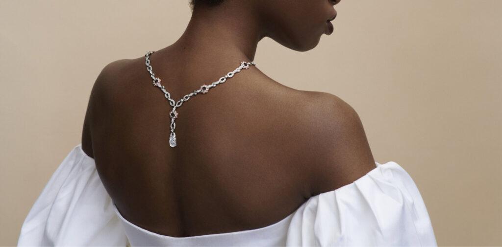 Model wearing a diamond necklace down the back with a white off-the-shoulder dress against a neutral background.