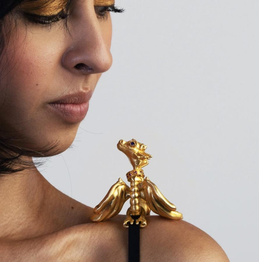 Close-up of a model wearing a sculptural gold dragon jewel with outstretched wings on her shoulder.