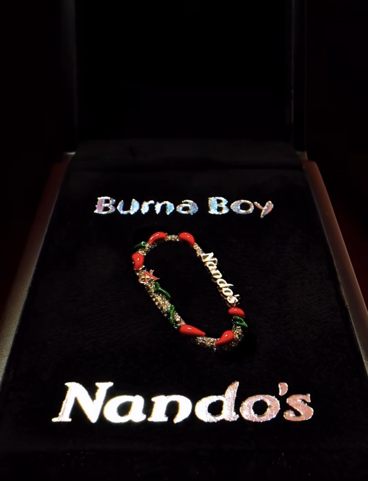 The custom white gold Nando’s clip for Burna Boy, fully set with diamonds and enamel chilli peppers, presented in a branded display case.