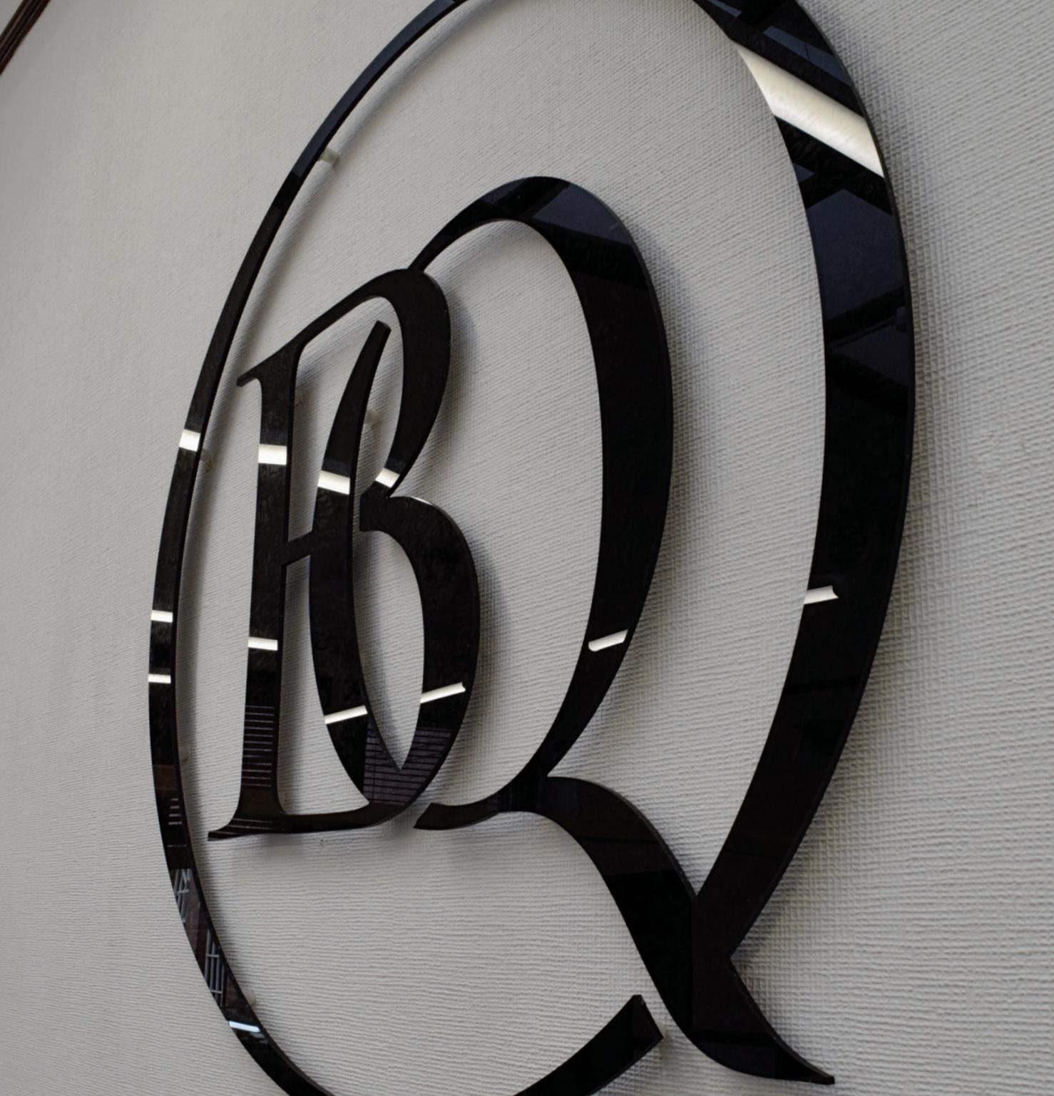 Close-up of the glossy black Bespoke Quarter monogram mounted on a textured white wall.