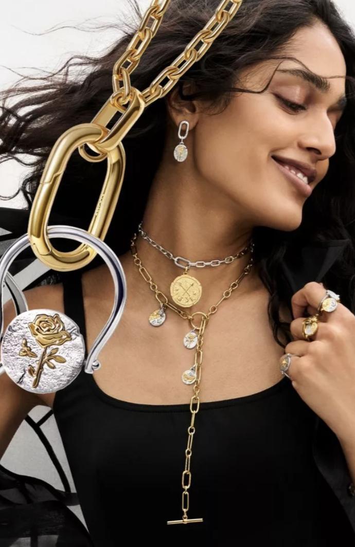Model wearing layered gold and silver Pandora Talisman necklaces, medallion rings and a drop earring with an enlarged rose charm shown beside her