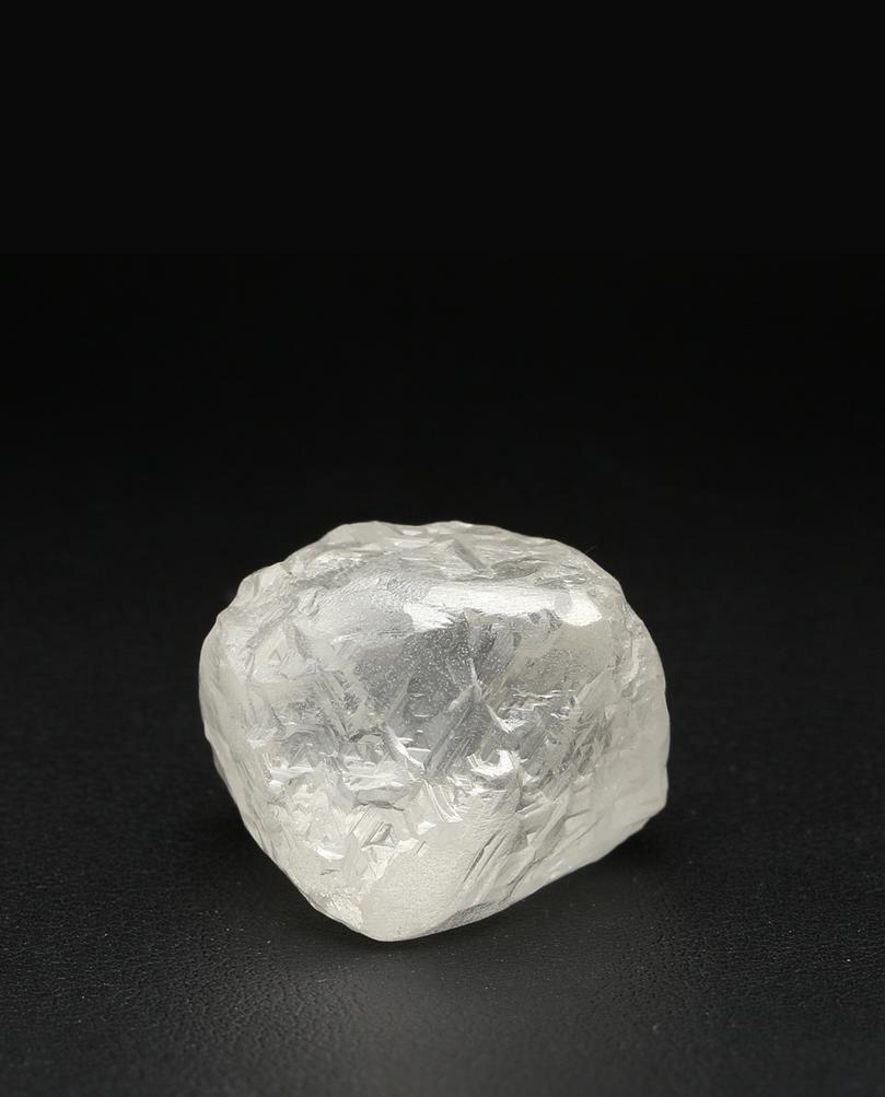 Large transparent rough diamond with an irregular cubic form photographed against a black background.