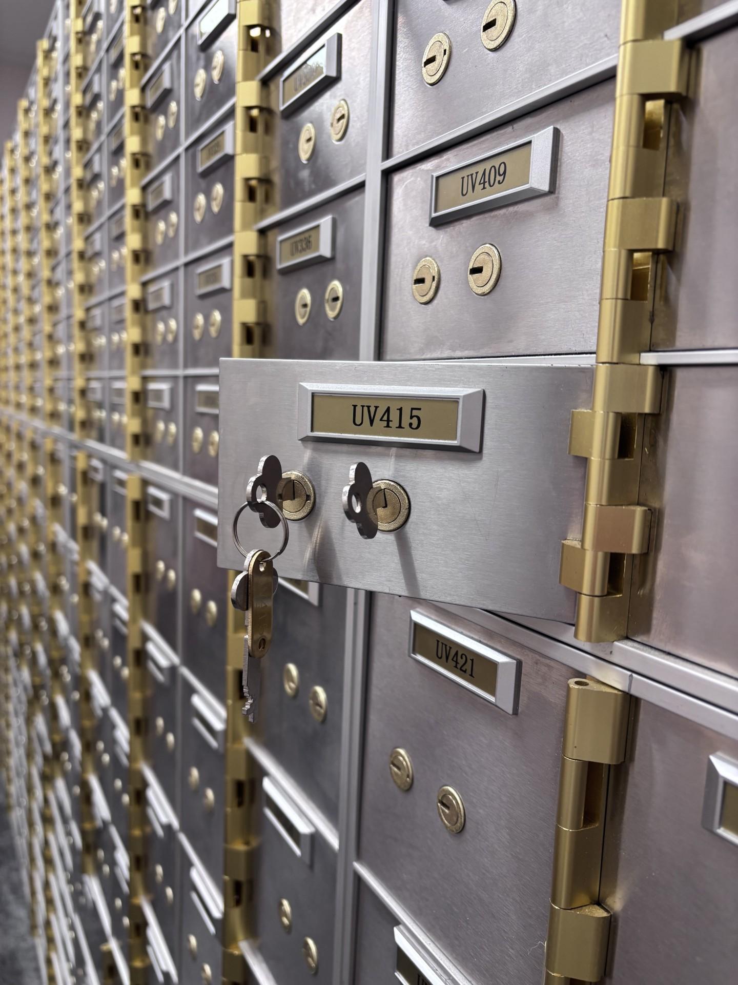 Rows of metal safe deposit boxes inside a secure vault facility, with one box partially open and keys inserted in the locks.