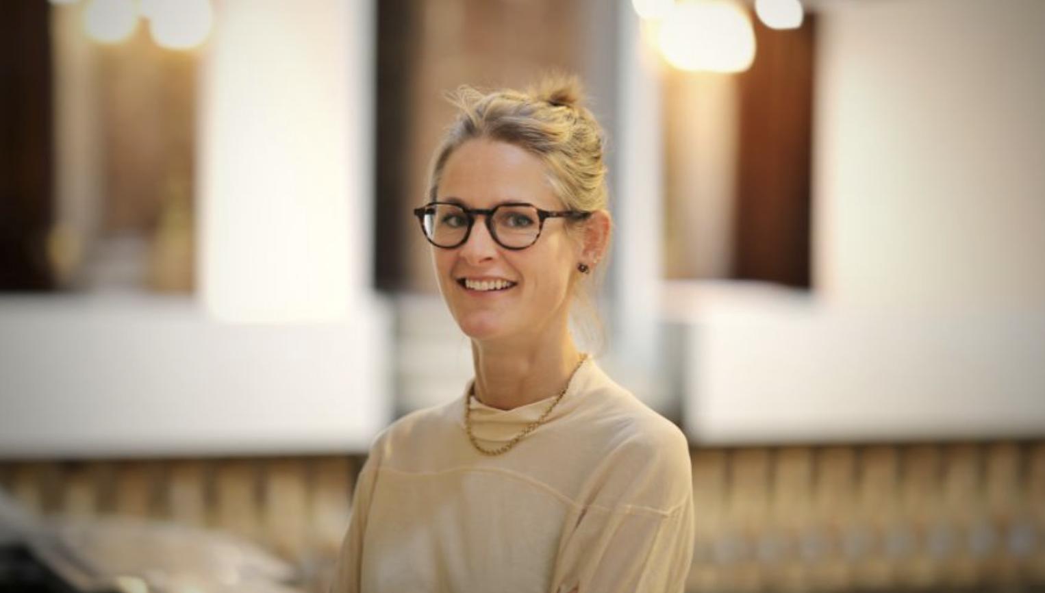 Portrait of Goldsmiths’ Fair Director Harriet Scott wearing glasses and smiling inside Goldsmiths’ Hall