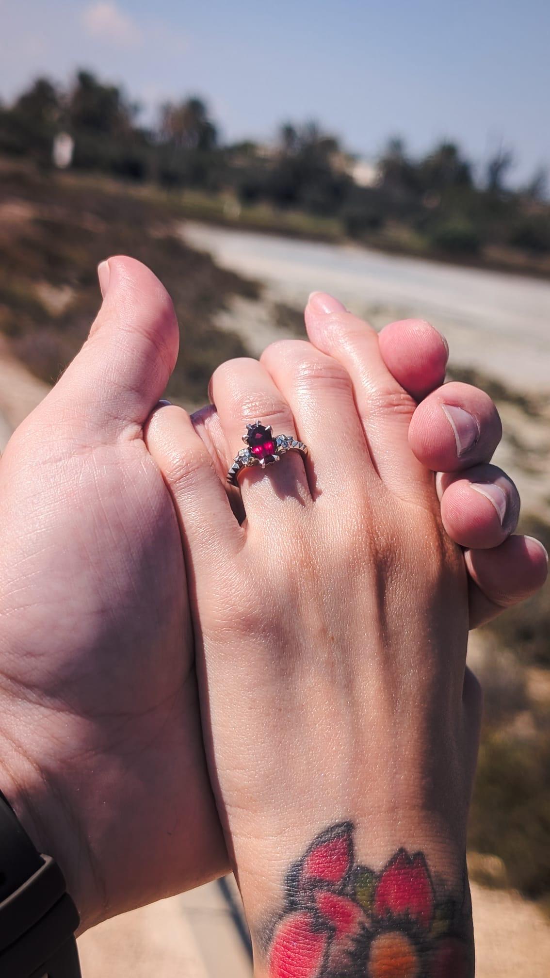 Paul and Leah holding hands outdoors after their engagement, with Leah wearing a white gold ring featuring a deep red coffin-cut garnet and diamonds.