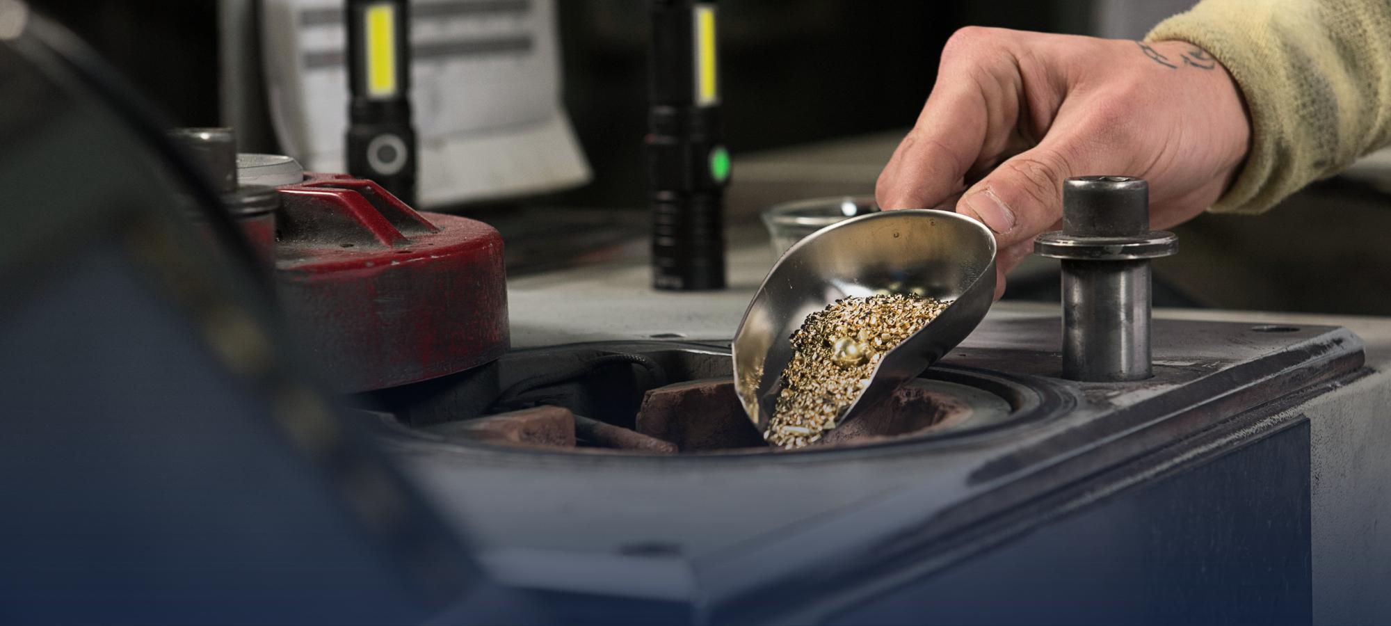 A Weston Beamor technician pours precious metal grain from a metal scoop into a casting crucible.