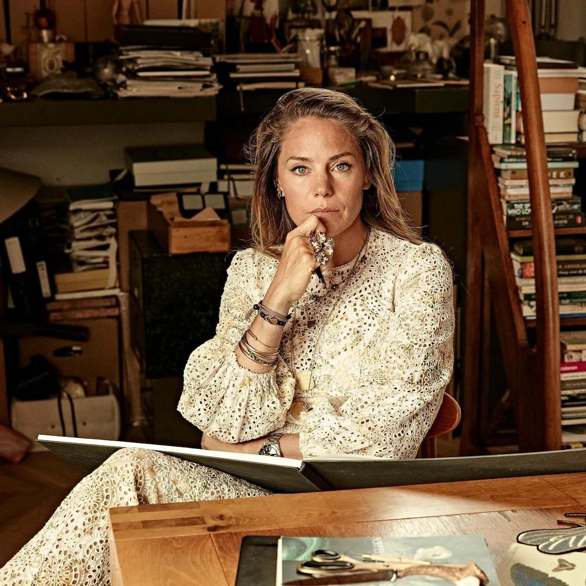 Bibi van der Velden seated in her studio surrounded by books and materials, wearing jewellery from her collection.
