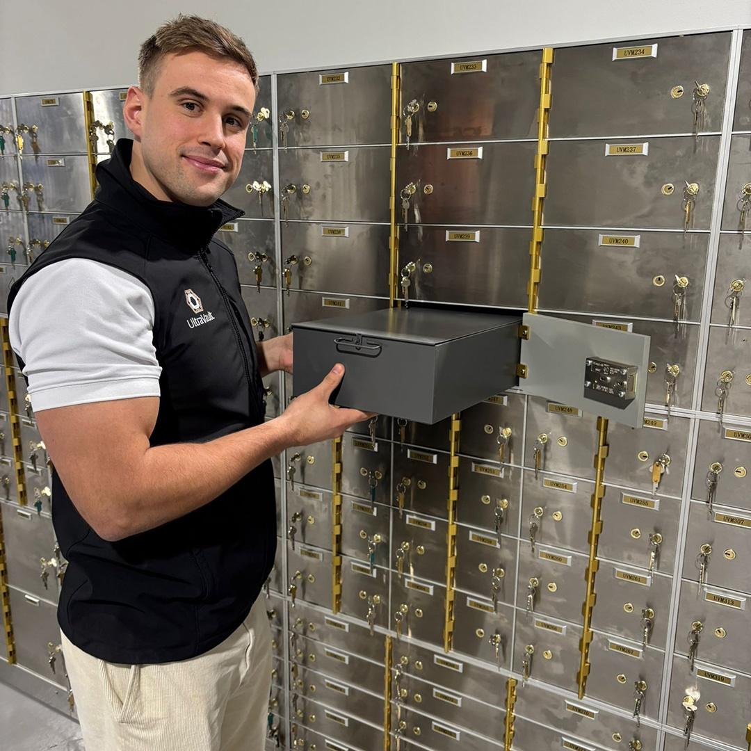 Will Brown holding a secure storage box inside UltraVault&rsquo;s Cheshire facility, standing in front of rows of metal safe deposit boxes.