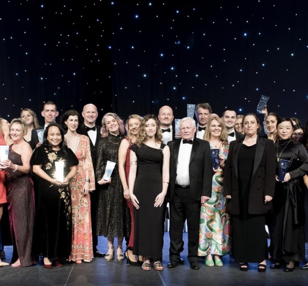 Winners of the NAJ Awards 2025 standing together on stage in evening dress, several holding trophies against a star-lit backdrop