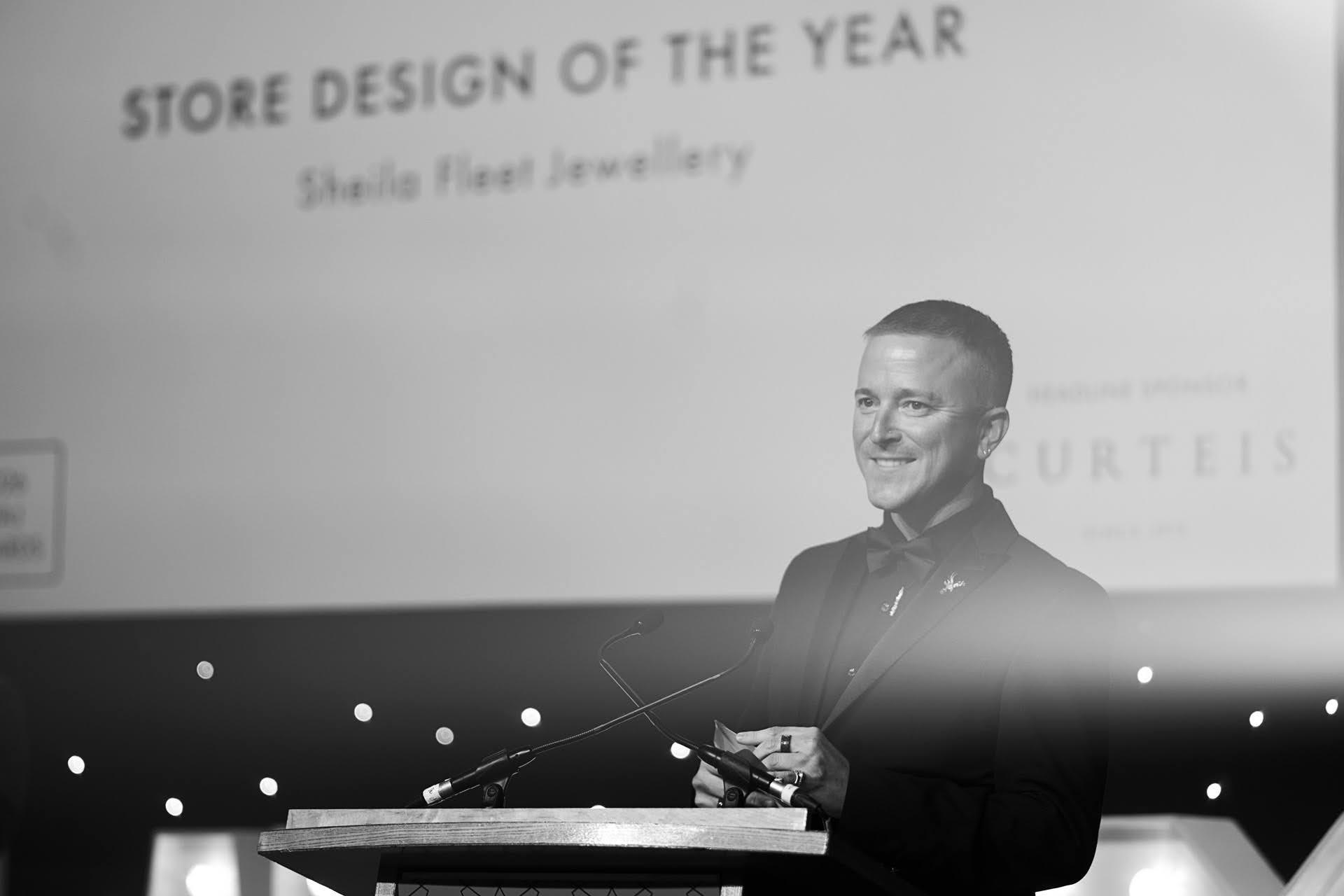 Andrew Martyniuk stands at the lectern announcing Sheila Fleet Jewellery as the winner of Store Design of the Year at the 2026 NAJ Awards