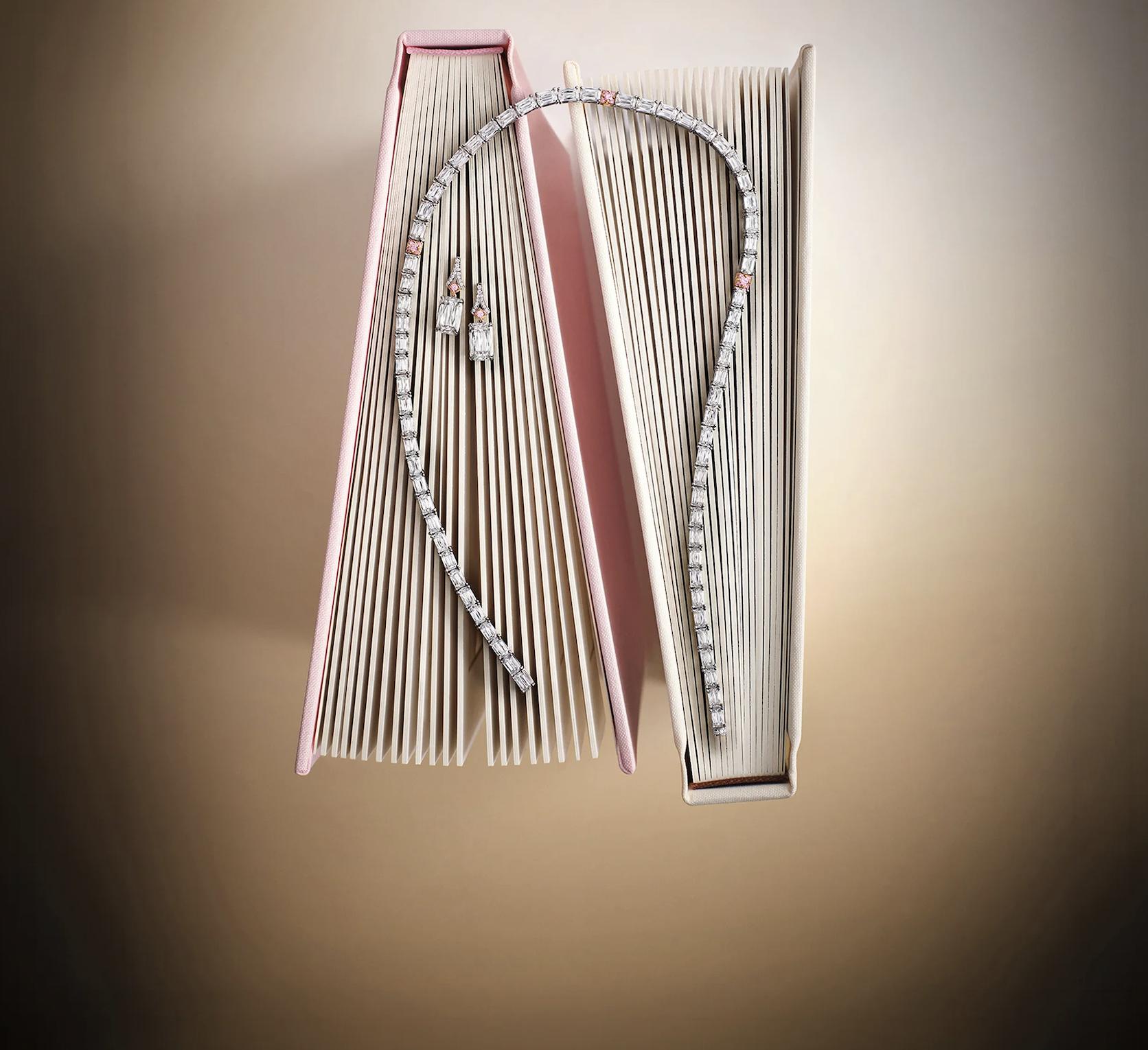 Ashoka-cut diamond necklace and drop earrings with pink diamond accents, arranged across two open books