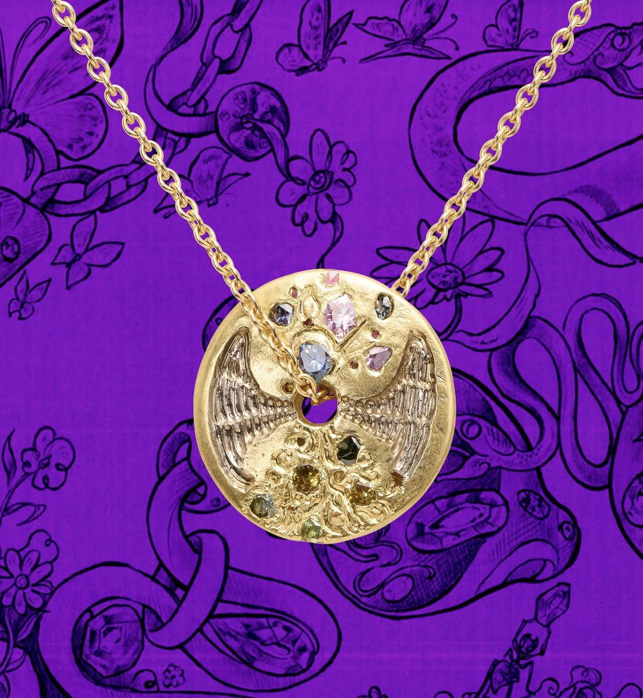 Gold pendant necklace from the Polly Wales x Castro Smith collection, featuring engraved wings, textured detailing and multicoloured gemstones against a purple illustrated background.