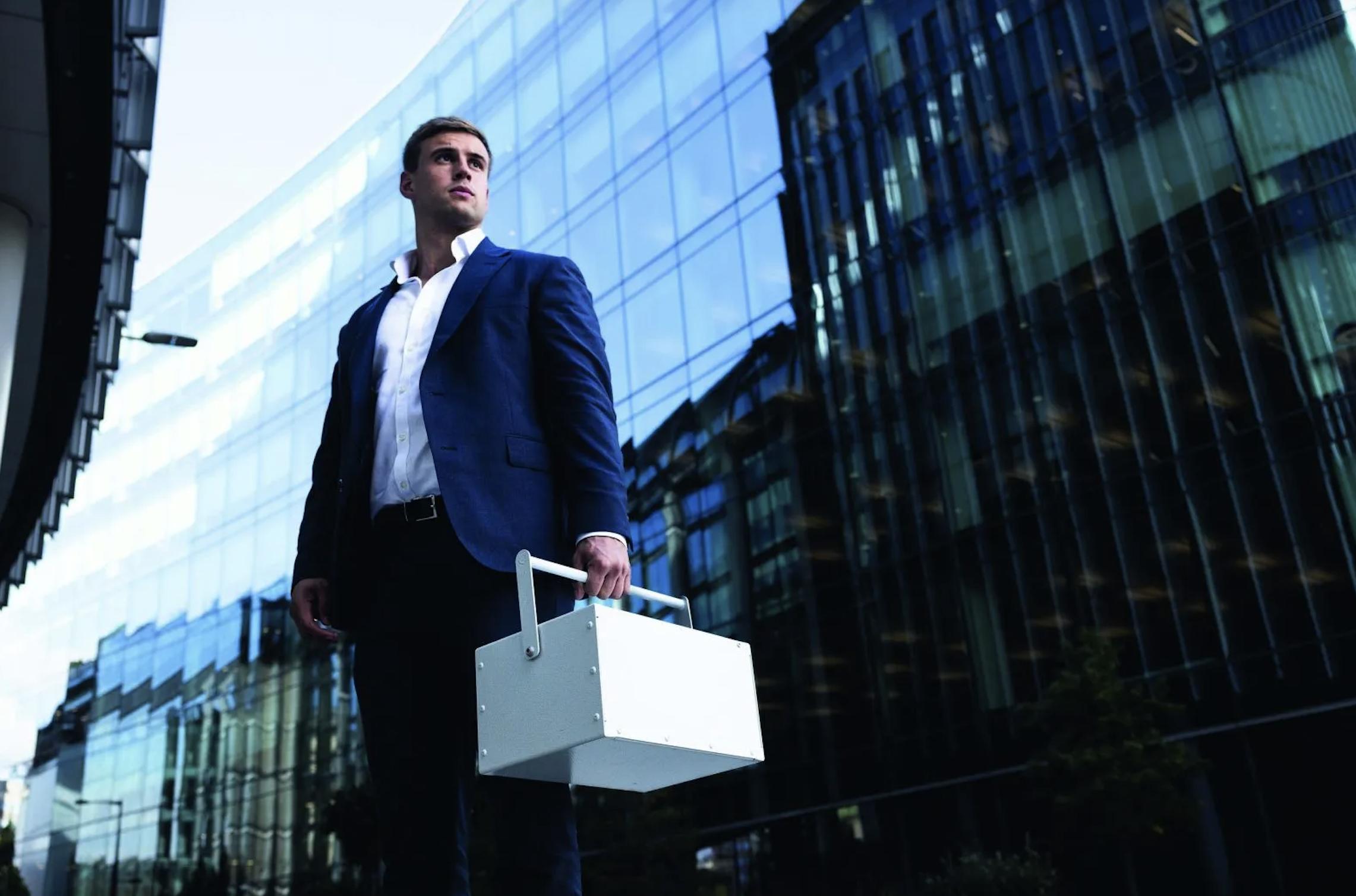 A man in a suit standing in a city setting holding a portable secure storage case, representing UltraVault&rsquo;s mobile vault service.