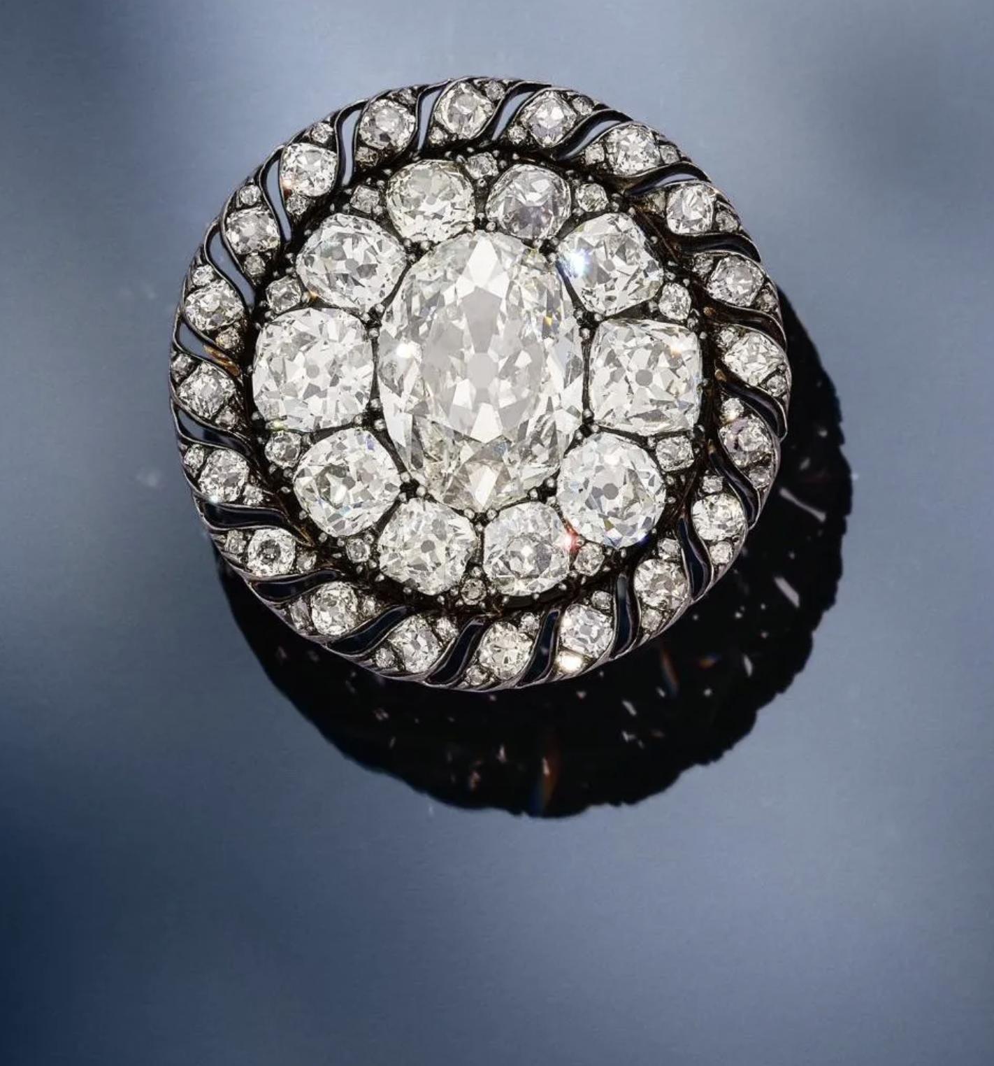 Circular antique brooch centred on a large oval old mine-cut diamond, surrounded by graduating diamonds in a dark metal setting