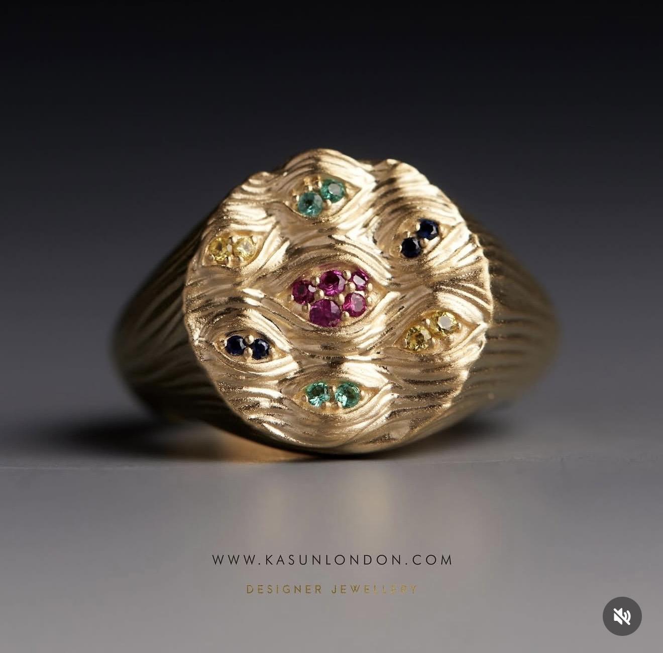 Textured gold ring from Kasun London’s Eyes of Many collection featuring eye-shaped motifs set with rubies, sapphires, emeralds and yellow gemstones across the face of the design.