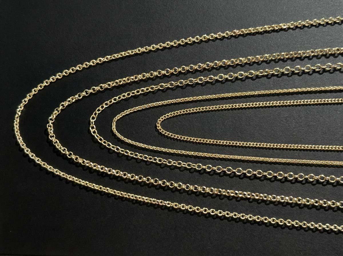 Gold chain styles including curb and trace designs laid out on a dark background