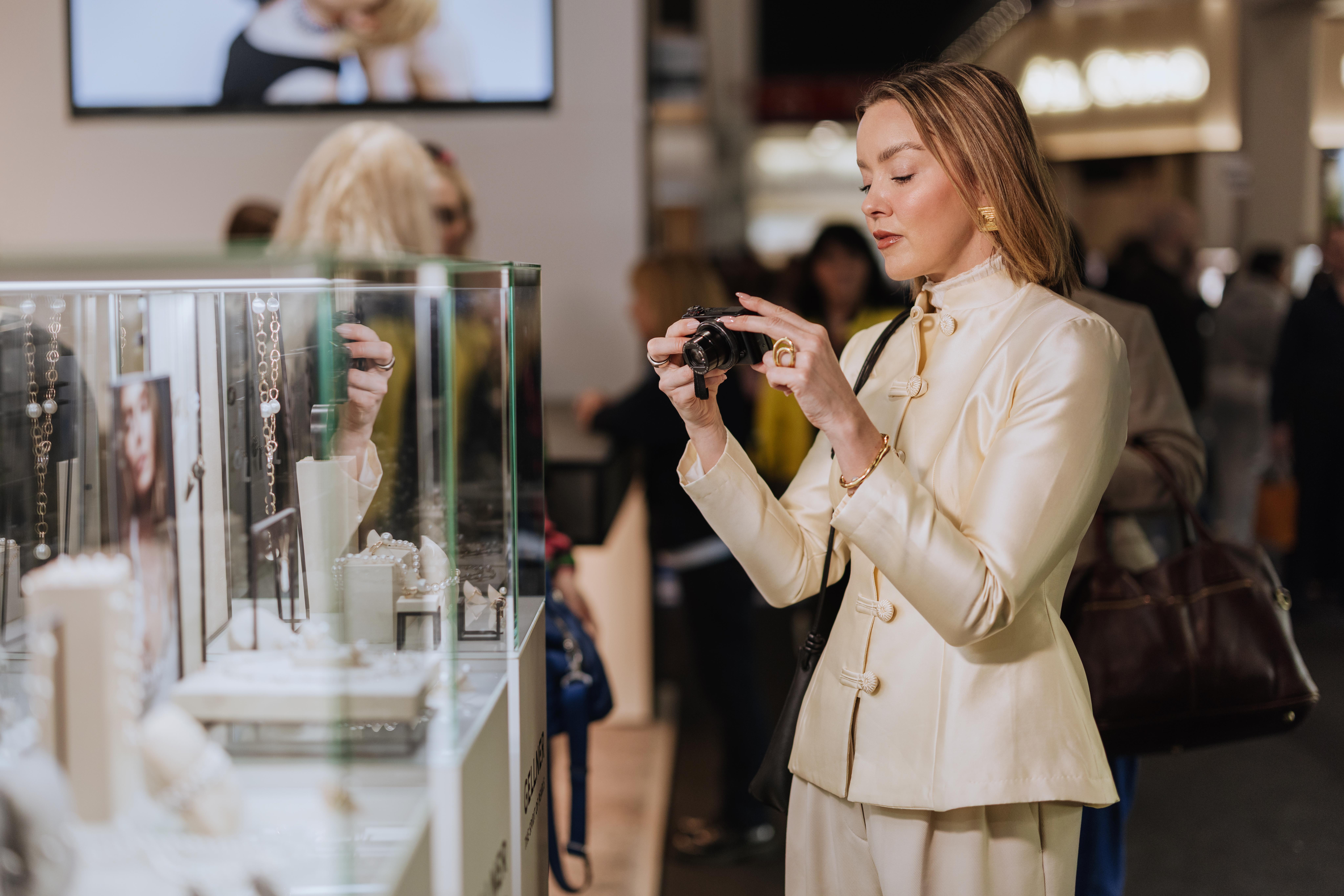 A visitor wearing a cream suit photographs jewellery displayed in a glass cabinet at INHORGENTA 2026