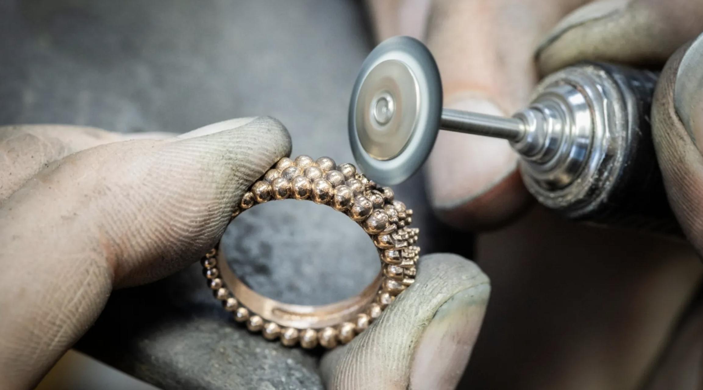 Jeweller polishing a rose gold Perlée-style ring with rounded gold beads using a rotating finishing tool in a workshop setting.