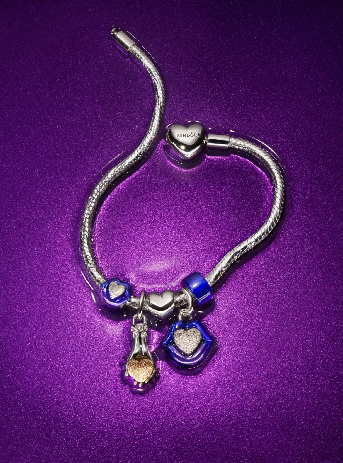Silver Pandora charm bracelet with blue enamel lips, a hand holding a gold heart and coordinating blue charms on a metallic purple background