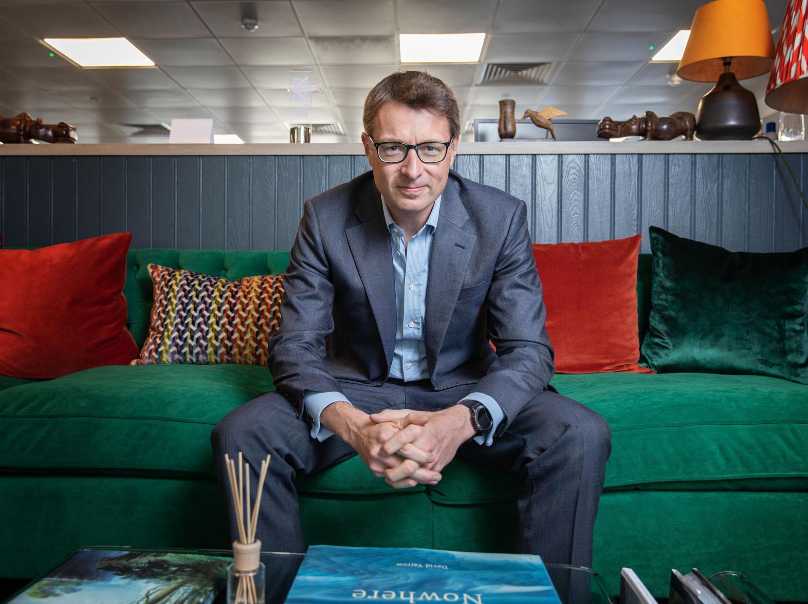 Portrait of Charlie Betts, Managing Director of The Betts Group, seated on a green sofa in an office setting