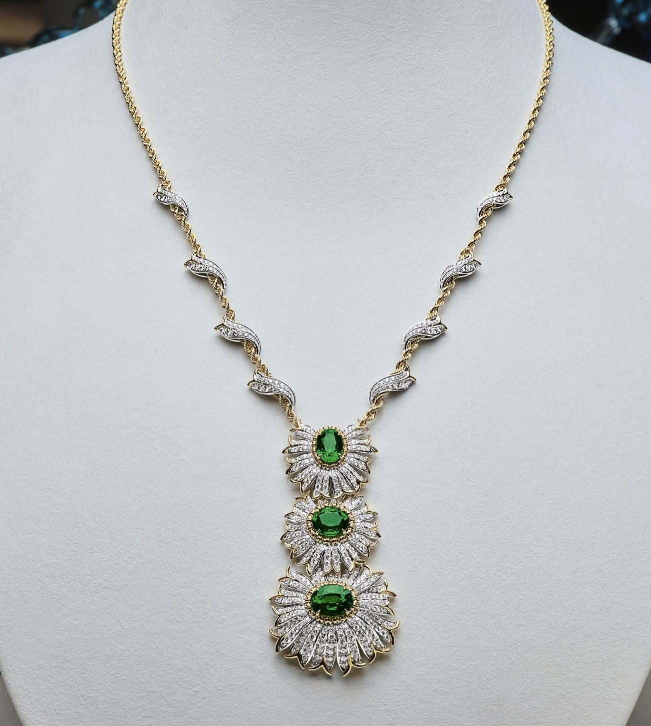 Tiffany Dahlia necklace with three green tsavorites surrounded by layered diamond petals on a white jewellery display.