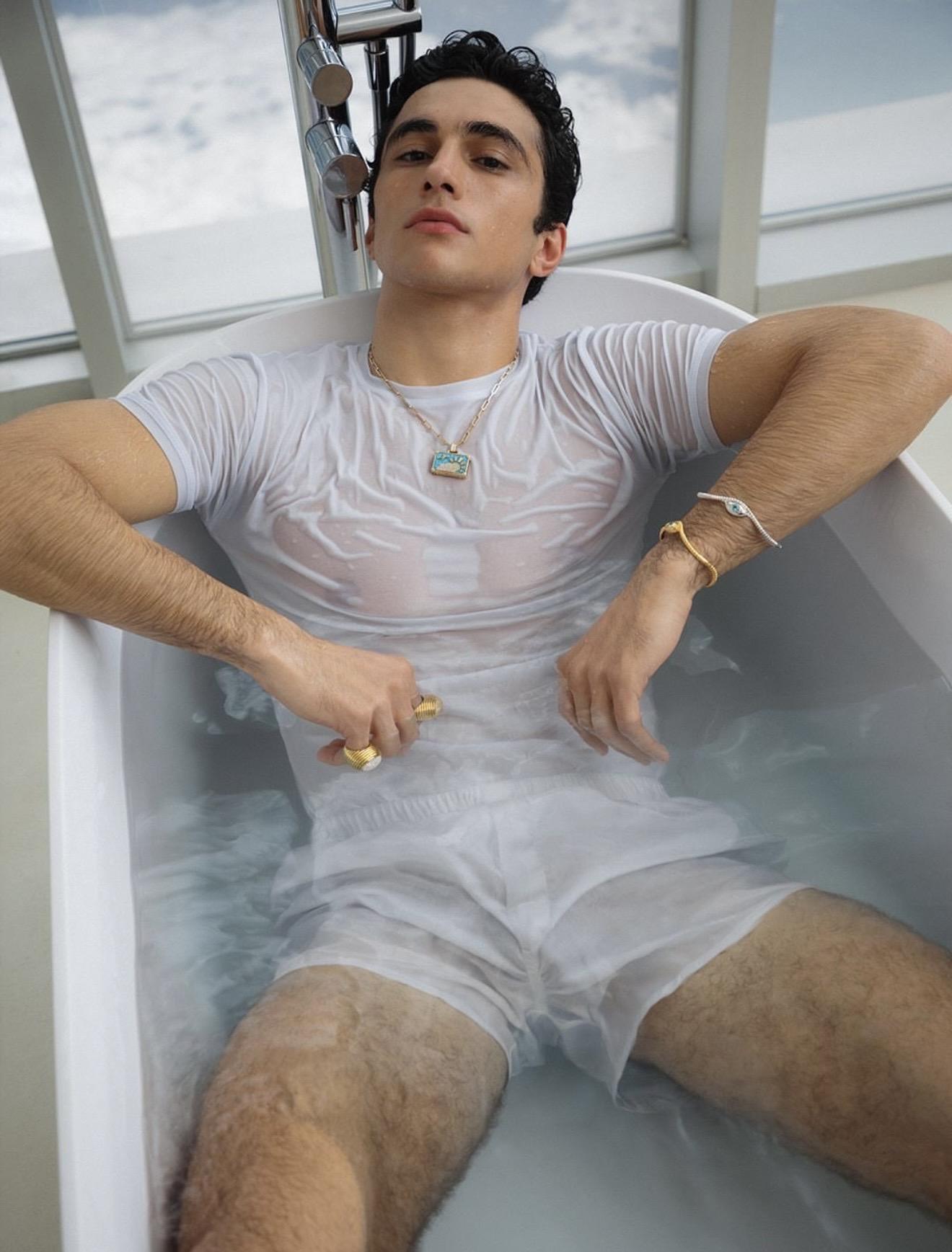 Model reclining in a bath wearing gold jewellery including a pendant necklace, rings and bracelet. NeverNot Jewellery