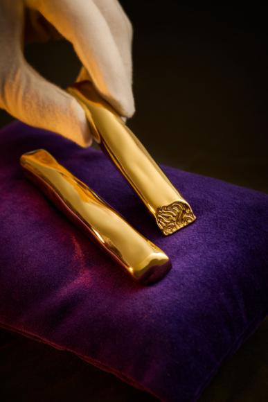 White-gloved hand lifting a gold-plated Twirl from a purple velvet cushion