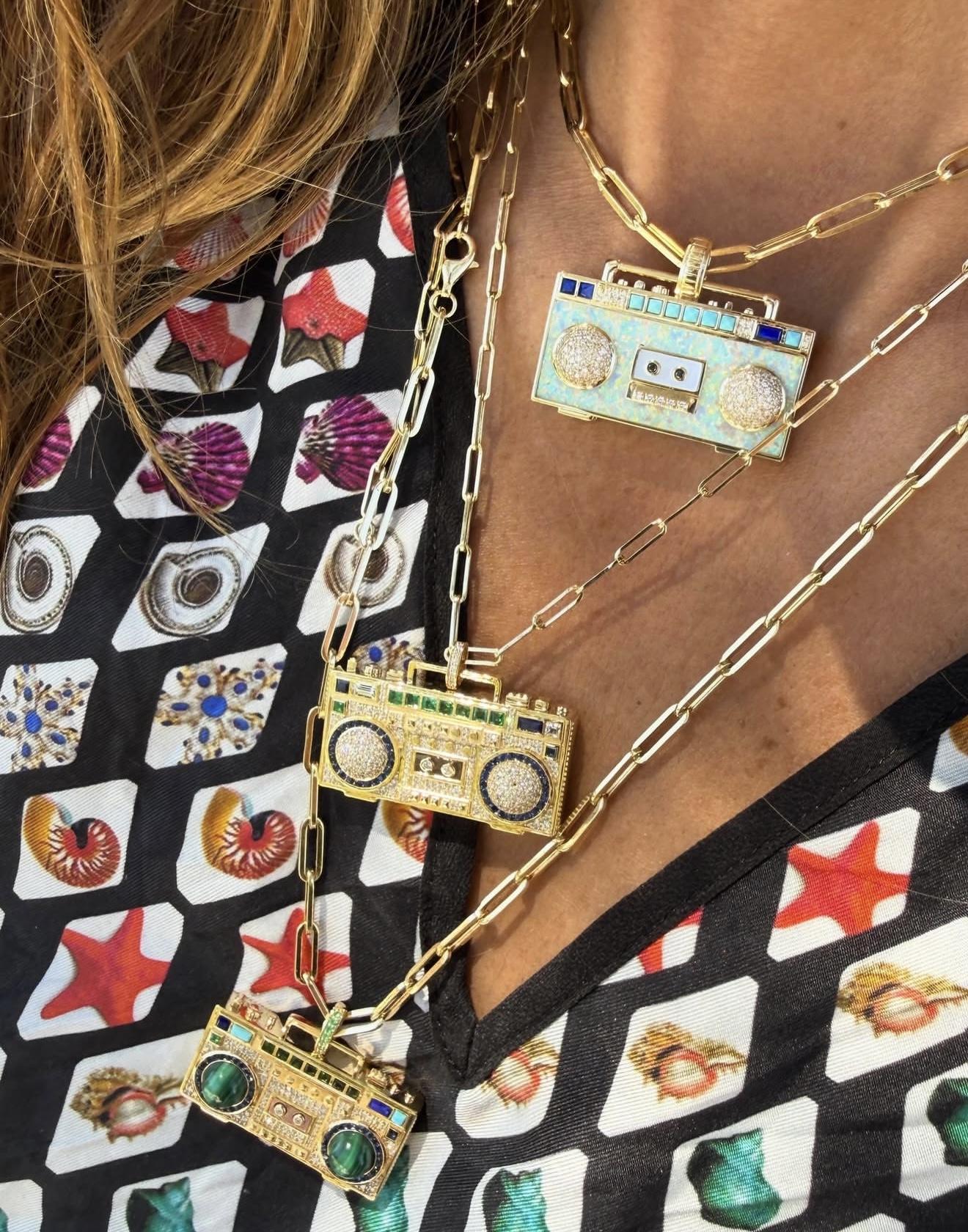 Three NeverNoT Turn It Up boombox pendants in yellow gold, diamonds and colourful gemstones worn on layered chain necklaces.