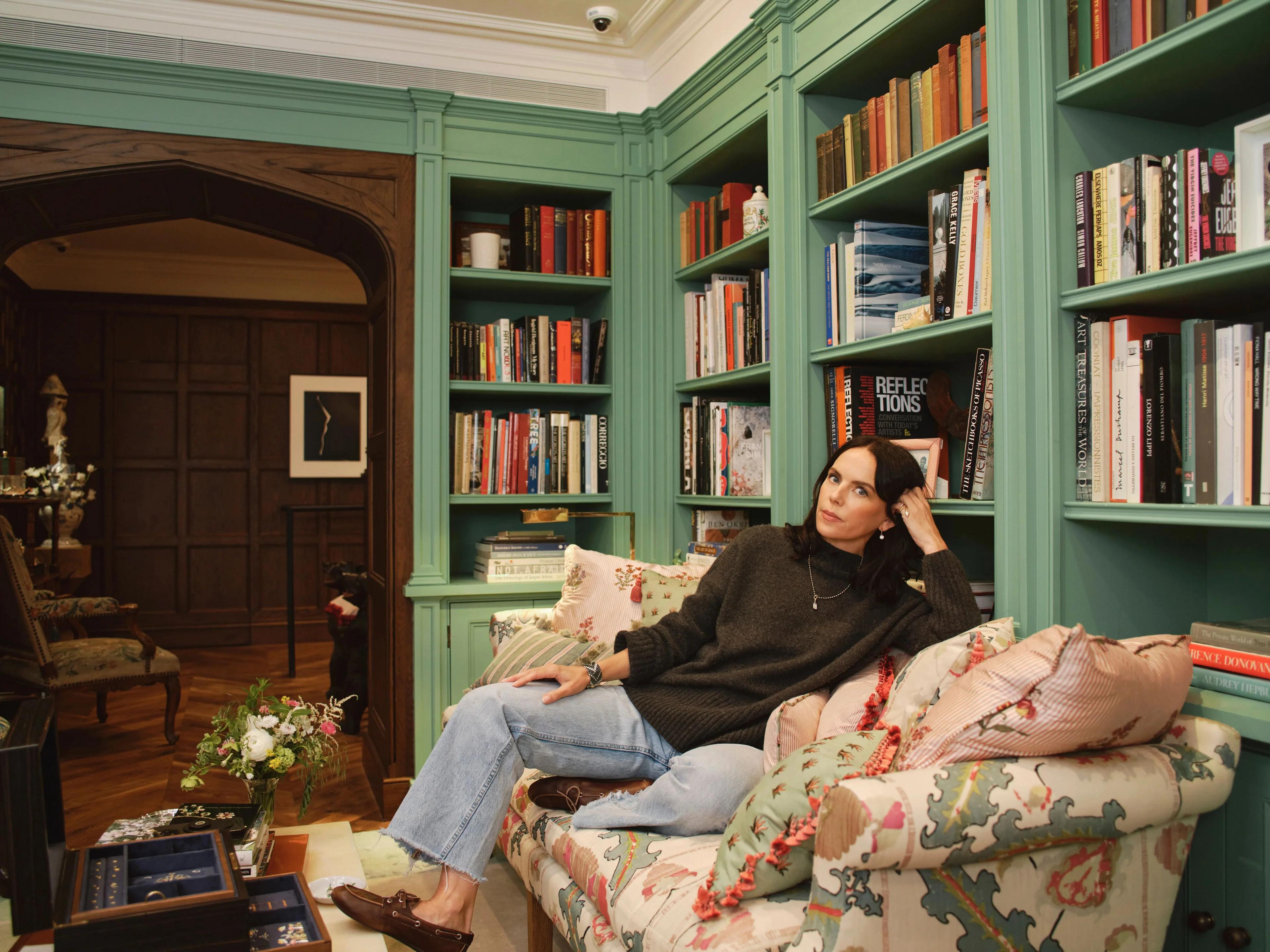 Jewellery designer Jessica McCormack seated in a library-style room at her London boutique surrounded by bookshelves and interiors reflecting her design aesthetic.