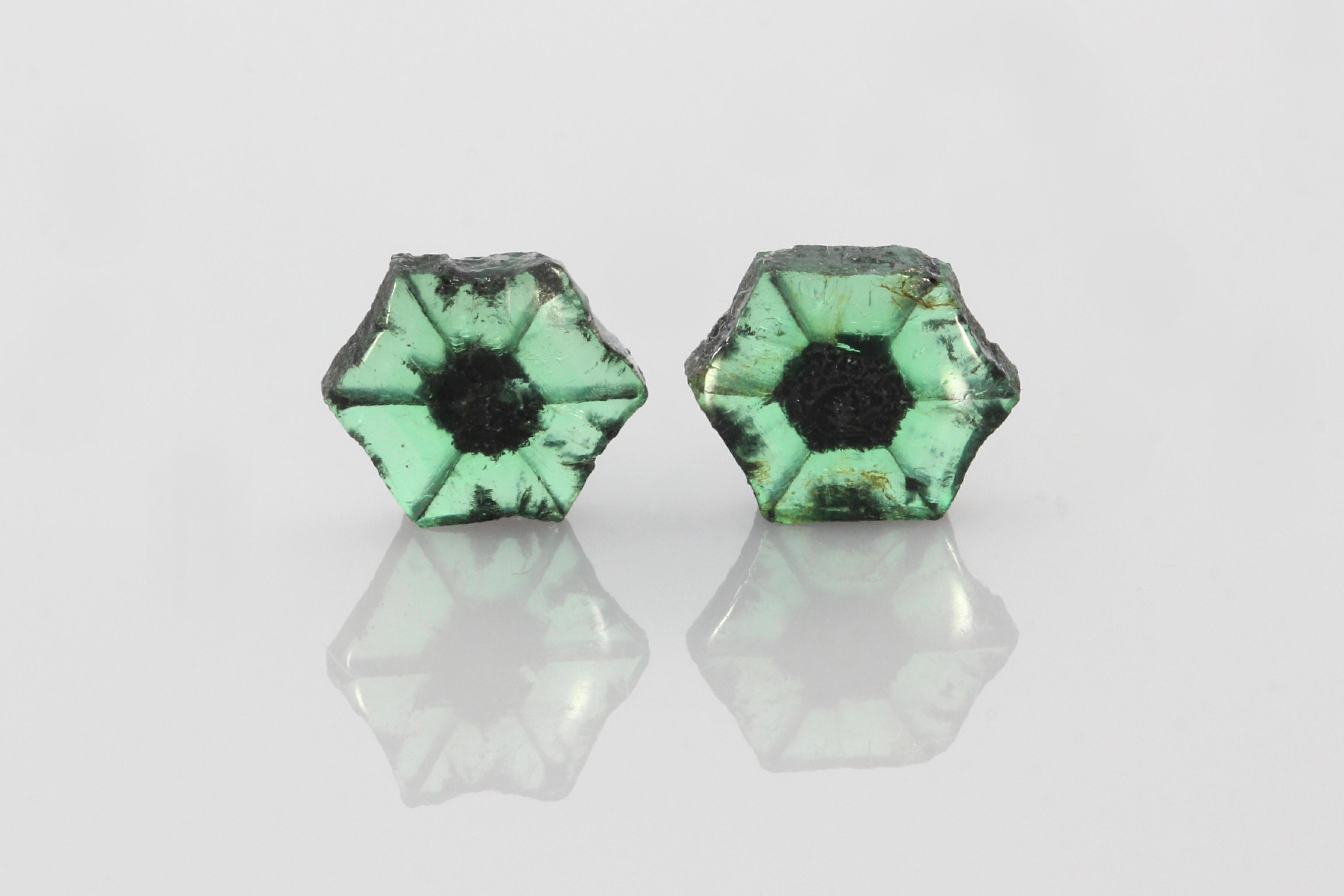 Close-up of two trapiche emeralds showing distinctive dark radial inclusion patterns against a white background.