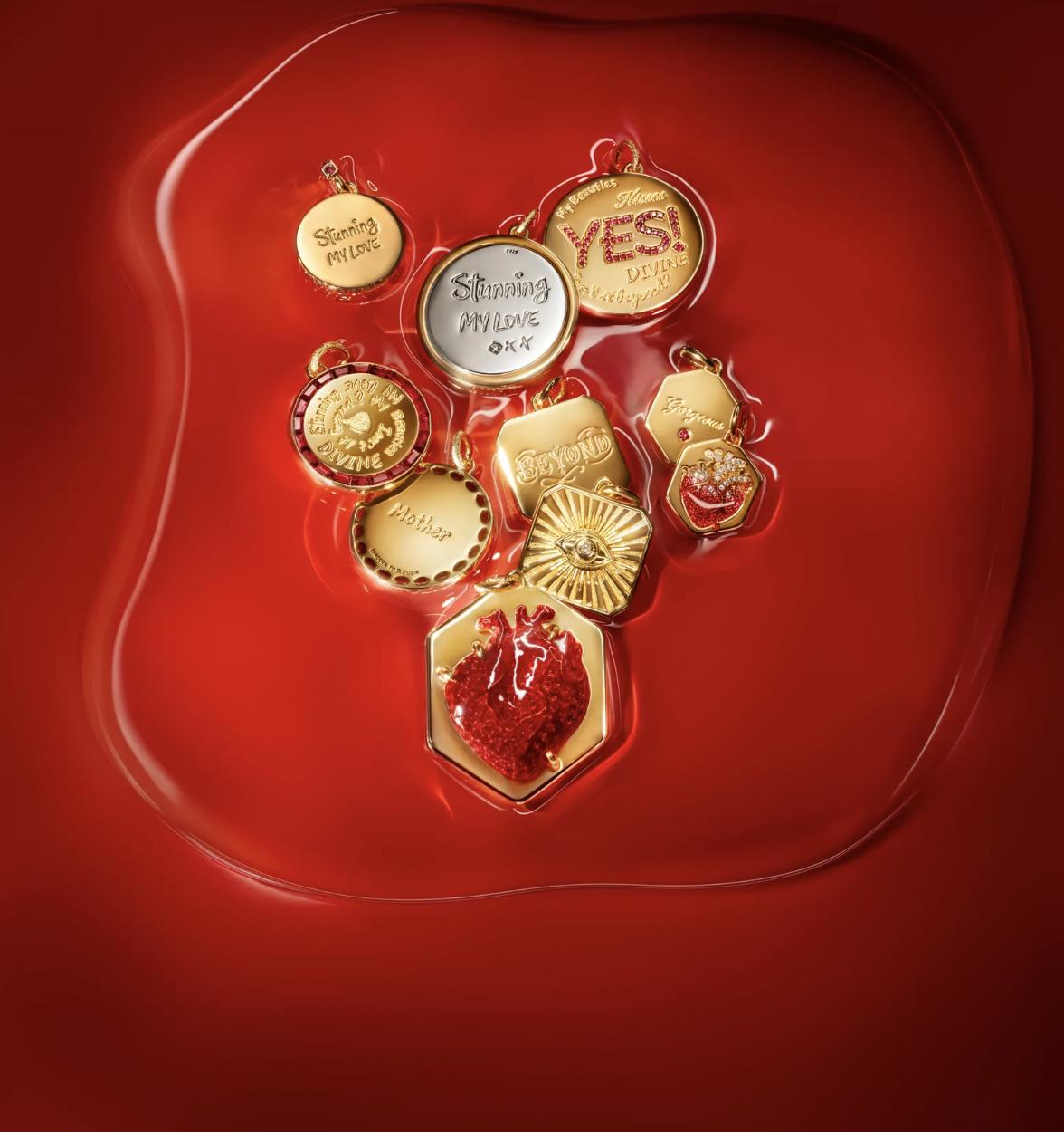 old-plated Pandora x Pat McGrath medallions with engraved phrases, a radiant eye, sparkling red lips and a red anatomical heart arranged on a glossy red surface