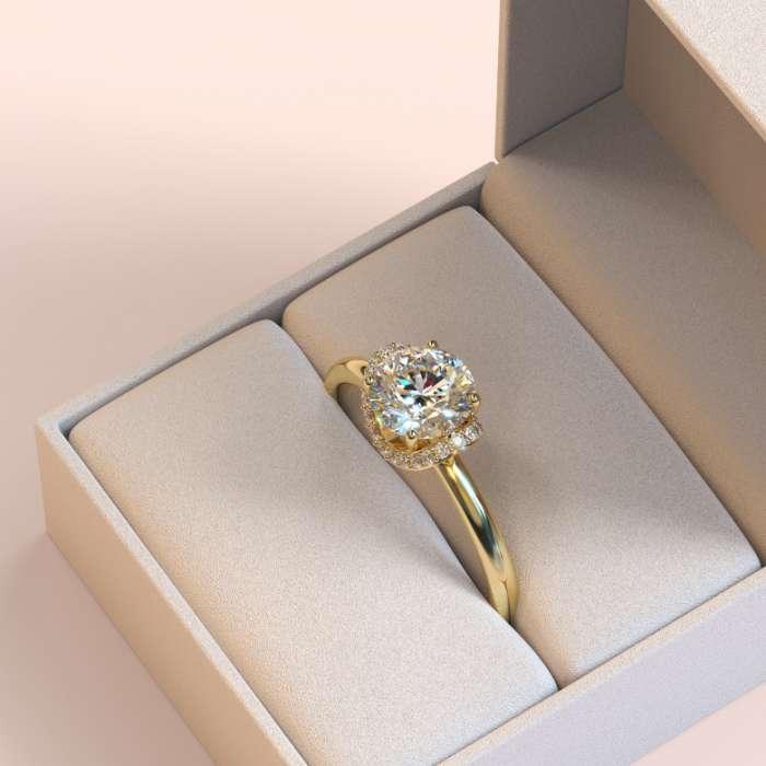 Yellow gold engagement ring with a round centre diamond and diamond halo displayed inside a pale jewellery box.