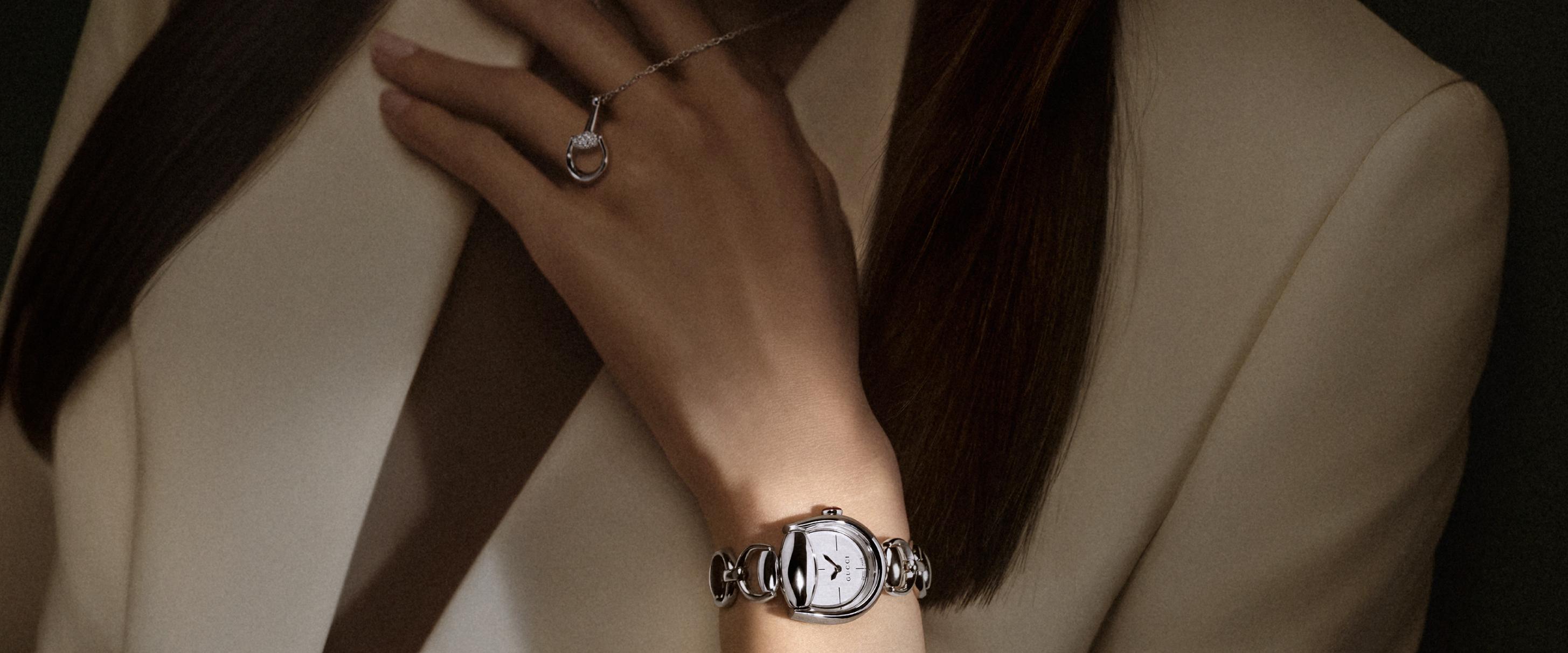 Model wearing a polished steel Gucci Horsebit watch with a silver dial and a diamond-set white-gold Horsebit pendant necklace