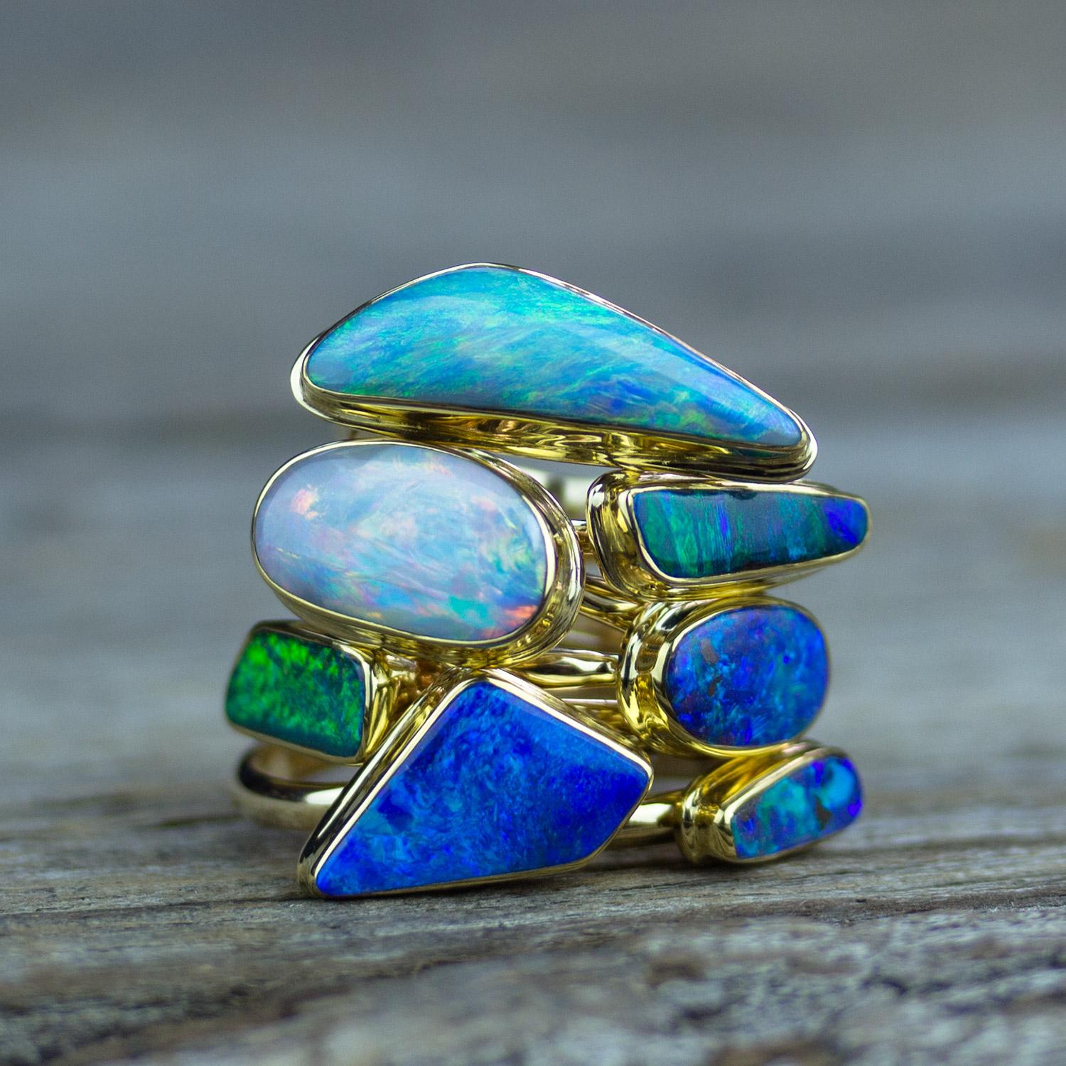 Stack of gold bezel-set rings featuring freeform opals in vivid shades of blue, green and iridescent white