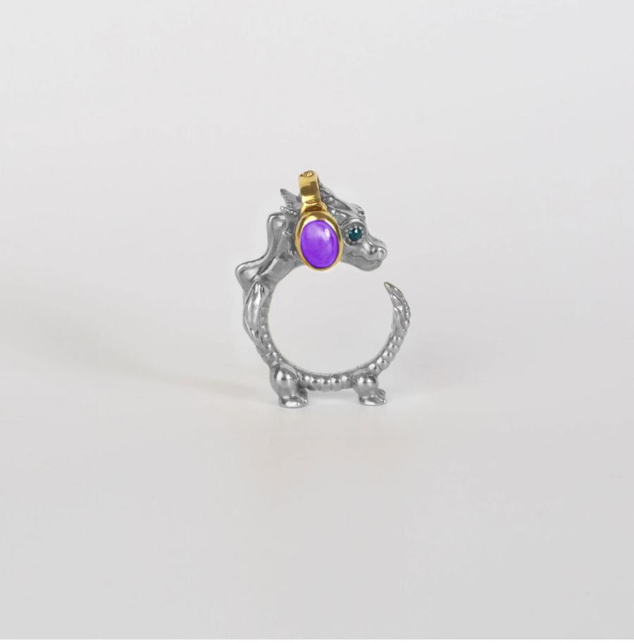 Small silver dragon ring standing upright on a white background, with a curled body, purple oval cabochon and blue gemstone eye.
