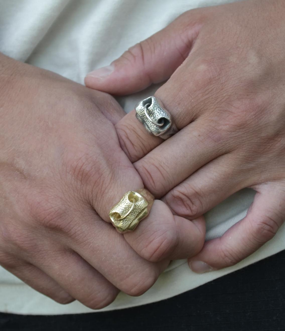 Close-up of two hands wearing textured animal Nose Rings by Kathryn Reid, one in silver and one in yellow gold, both with movable hoops through the nostrils