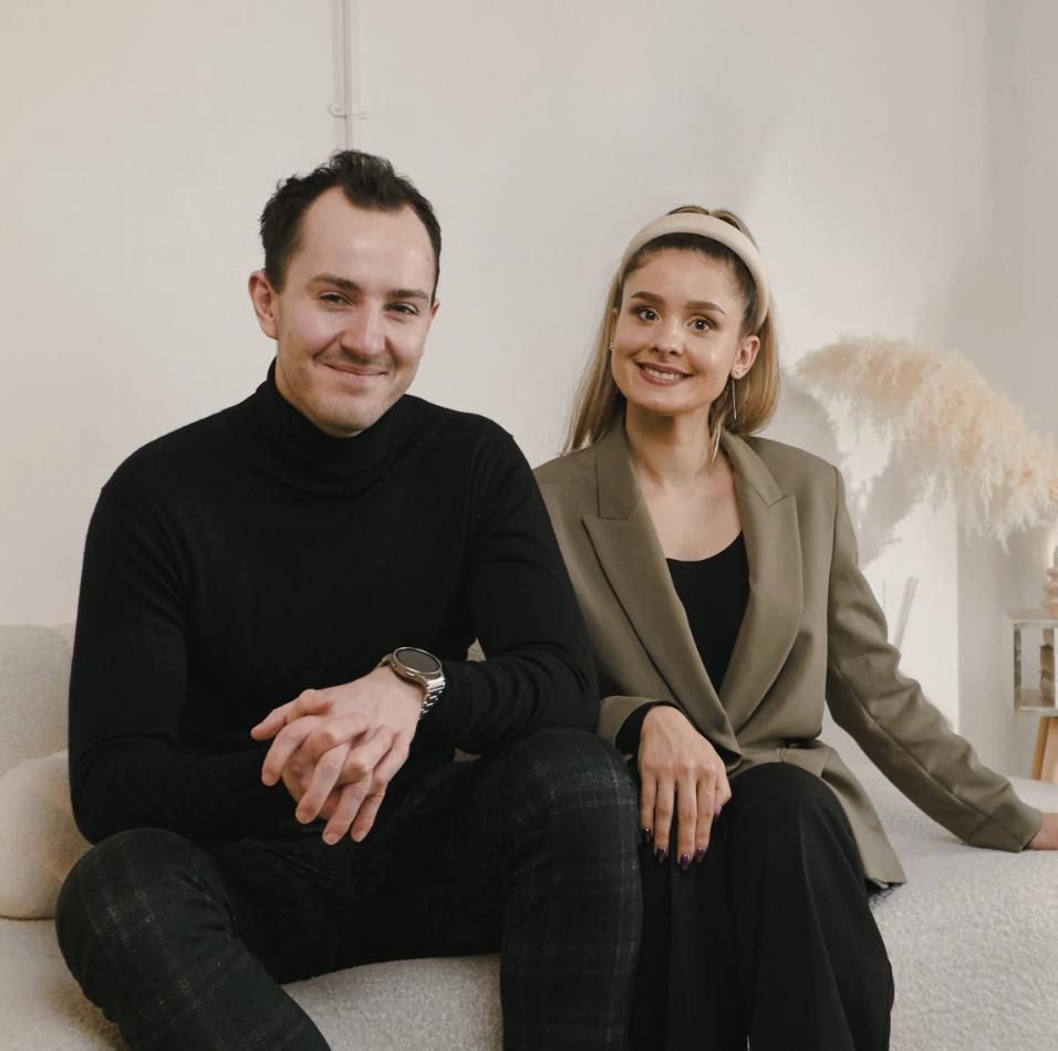 AUZI co-founders Dec and Daniela seated together on a cream sofa, smiling at the camera