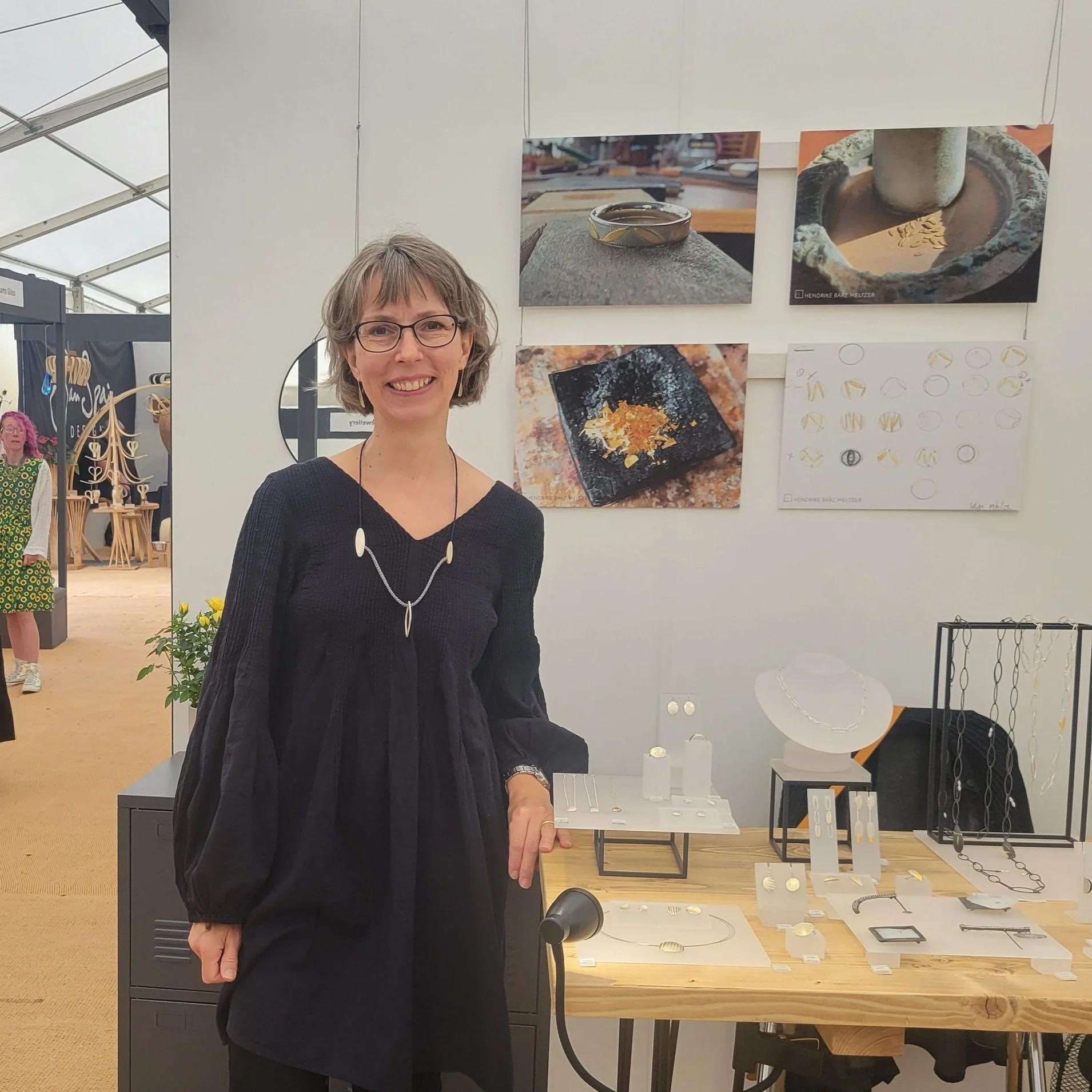 Hendrike Barz-Meltzer standing beside a display of her silver and gold jewellery and photographs of the making process