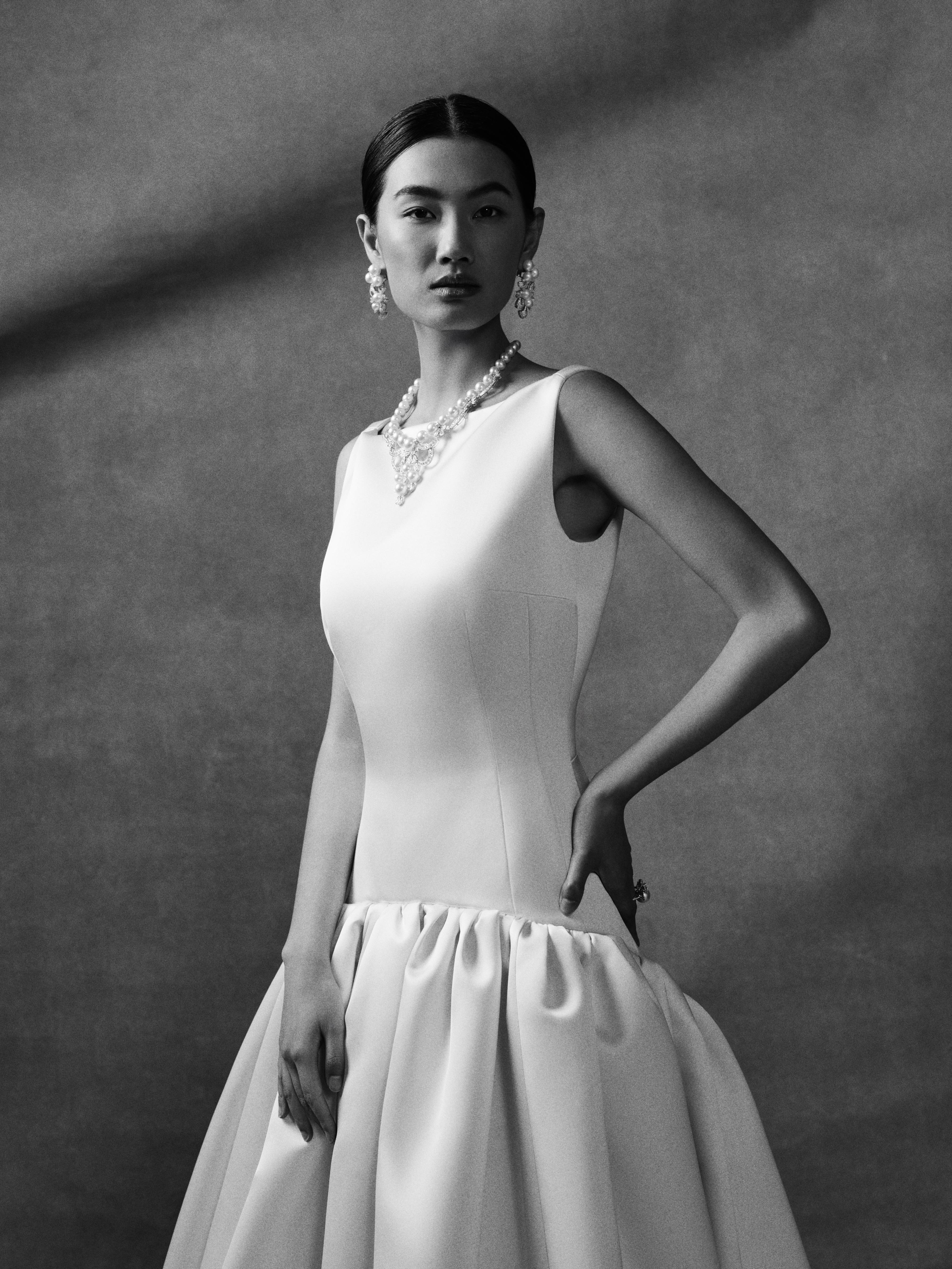 Model wearing a sleeveless white bridal gown styled with a statement pearl necklace, matching pearl earrings and a ring from the Yoko London x Emilia Wickstead bridal collection, photographed in a monochrome portrait setting