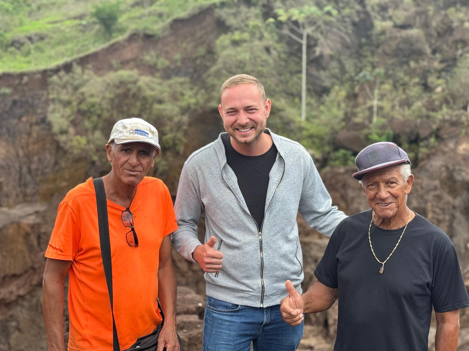 Tobias Kempf of TK Collection with two local gemstone miners at a Brazilian mine, smiling and giving a thumbs up at the rocky site.