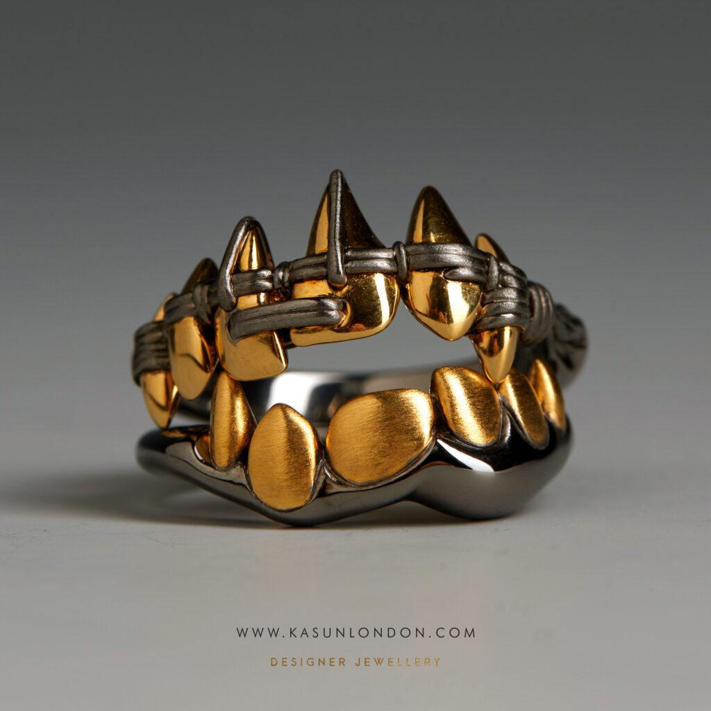 Two sculptural Kasun London rings resembling rows of gold teeth and pointed fangs, set against a grey background