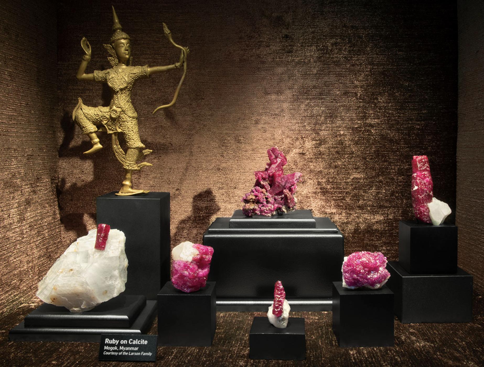 Display of ruby crystals on white marble from Mogok, Myanmar, showcased alongside additional ruby specimens.