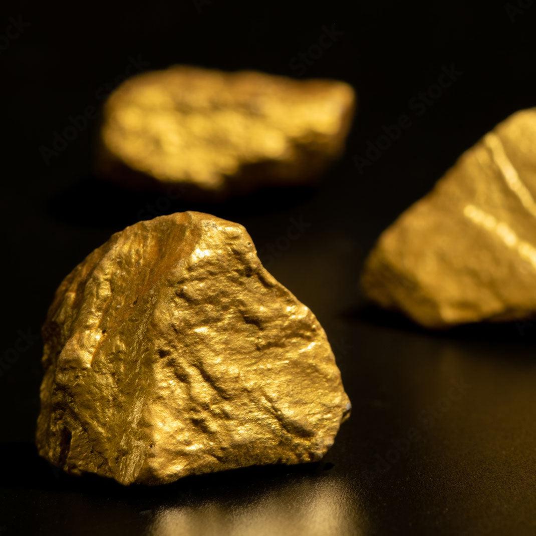 Close-up of raw gold nuggets on a dark reflective surface.