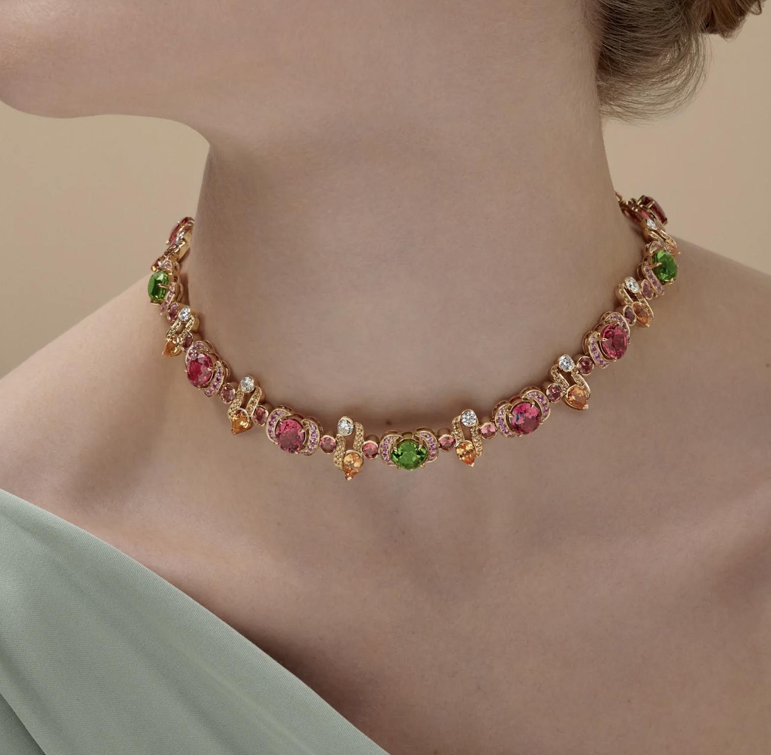 Close-up of a model wearing a yellow gold necklace set with pink, green, orange and white gemstones.