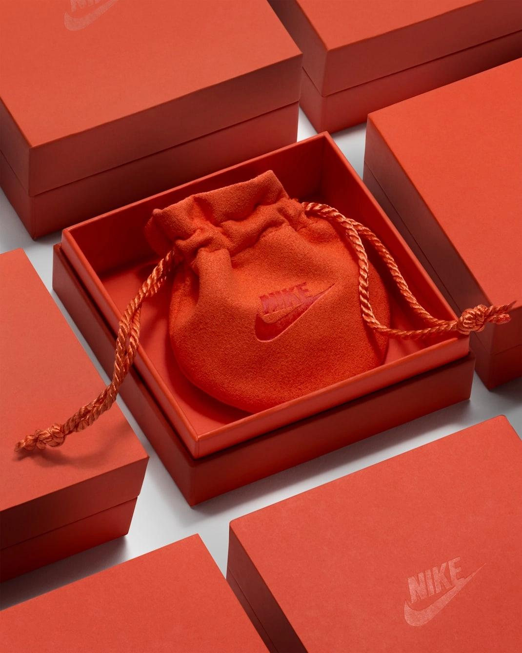Red Nike jewellery boxes arranged around an open box containing a matching drawstring pouch embroidered with the Nike Swoosh.