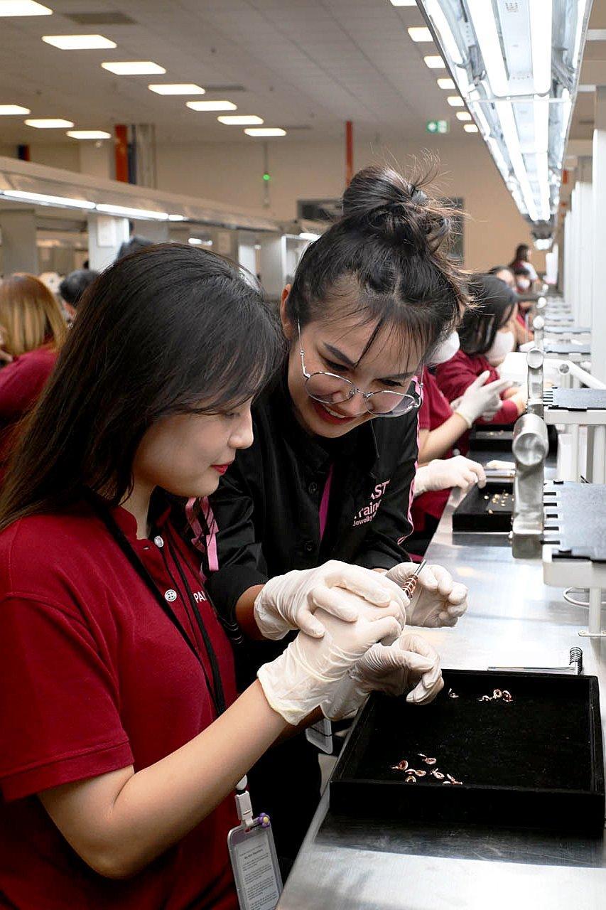 Two Pandora craftspeople wearing protective gloves examine small jewellery components at a brightly lit production workstation