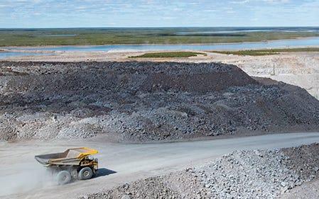 Yellow mining haul truck travelling along a road between rock piles at the Gahcho Kué diamond mine.